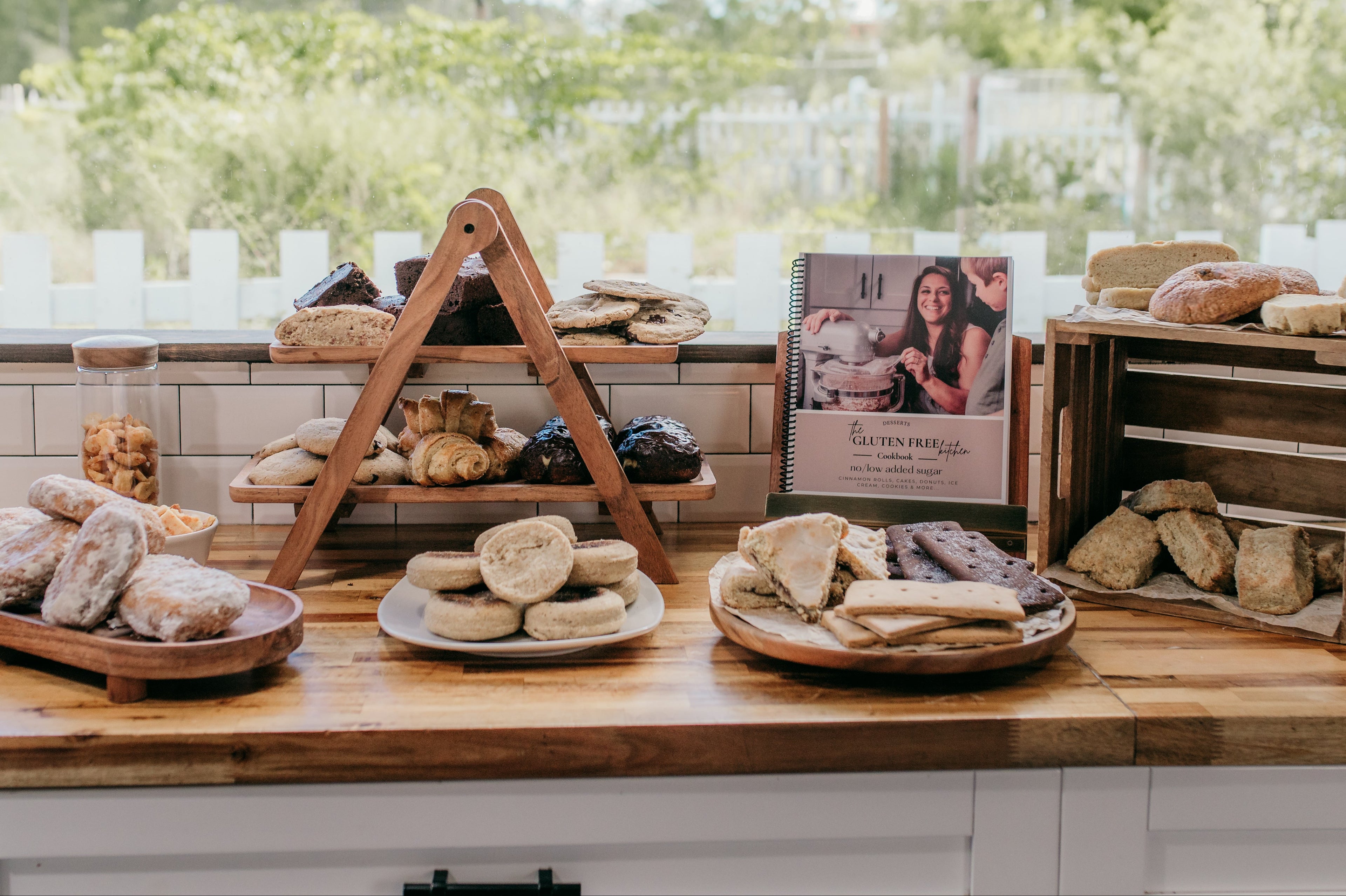 a countertop filled with gluten free treats like beignets, croissants, goldfish, pop tarts, graham crackers, bagels, biscuits, English muffins, cookies, brownies and a cookbook. The cookbook shows Jennifer Roberts, author of The Gluten Free Kitchen Series.
